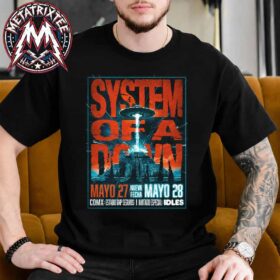 A man sitting on a couch wearing a black System Of A Down 2 Nights In CDMX 2026 Poster Short T-Shirt featuring a sci-fi concert graphic with a UFO beaming a light down.