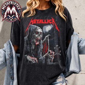 A model wearing a dark gray metallica glasgow washed shirt featuring a grim reaper graphic in front of a graveyard.