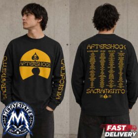 man wearing a black aftershock 2026 long sleeve shirt with festival lineup on the back and yellow logo on the chest against a concrete wall.